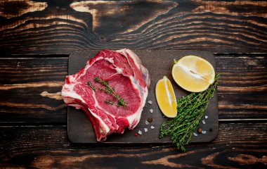 Ahşap arka plan üzerinde biberiye ve limon dilimleri ile Çiğ yağ domuz biftek 