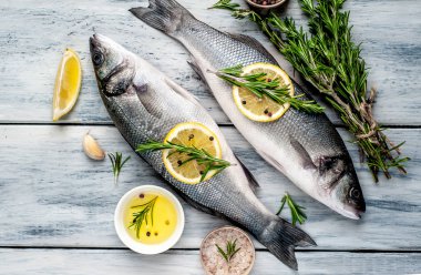 Gri ahşap arka plan üzerinde limon dilimleri ve biberiye dalları ile çiğ balık