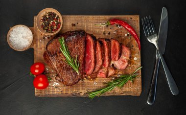 Taze sığır eti biftek ahşap tahta üzerinde domates, biberiye biberiye ve biberiye dalları ile servis