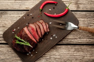 Ahşap arka planda baharat ve biberiye dalları ile taze ızgara biftek