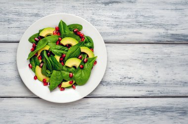 Ahşap masada ıspanak yaprakları, avokado dilimleri ve nar taneleri ile taze yeşil salata 