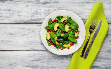 Ahşap masada ıspanak yaprakları, avokado dilimleri ve nar taneleri ile taze yeşil salata 