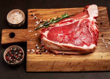 Taş arka plan üzerinde ahşap doğrama tahtası üzerinde baharat ve biberiye dal ile Çiğ yağlı biftek