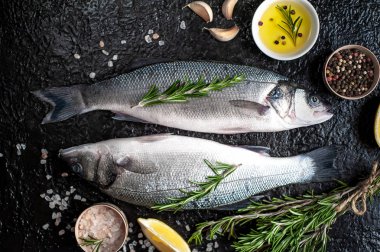 Siyah taş arka plan üzerinde limon, baharat ve biberiye dalları ile çiğ balık