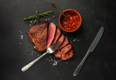 Dilimlenmiş taze sığır eti biftek taş arka plan üzerinde domates sosu ve biberiye dal ile servis