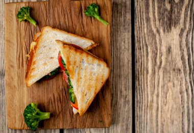 Ahşap doğrama tahtasında jambon, taze brokoli ve peynirile taze ızgara sandviçler