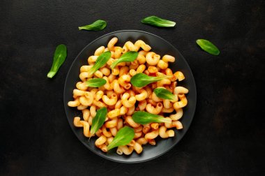 taş siyah arka plan üzerinde yeşil yaprakları ile servis domates soslu makarna