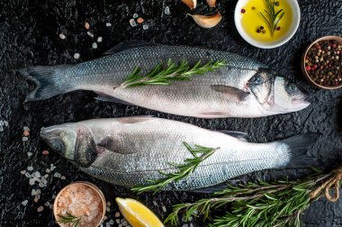 Siyah taş arka plan üzerinde limon, baharat ve biberiye dalları ile çiğ balık