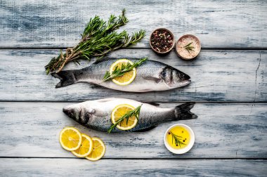 Gri ahşap arka plan üzerinde limon dilimleri ve biberiye dalları ile çiğ balık
