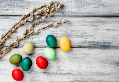 Beyaz ahşap arka planda renkli Paskalya yumurtaları ve kedi söğüt dalları yığını