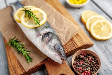 Ahşap doğrama tahtası üzerinde limon dilimleri ve biberiye dalları ile çiğ balık