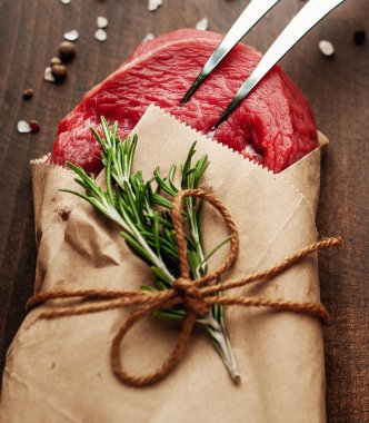 Ahşap doğrama tahtası üzerinde biberiye dalları ile zanaat kağıt sarılmış çiğ sığır eti biftek