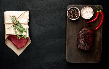 Izgara biftek ve çiğ et siyah taş arka plan üzerinde zanaat kağıt sarılmış