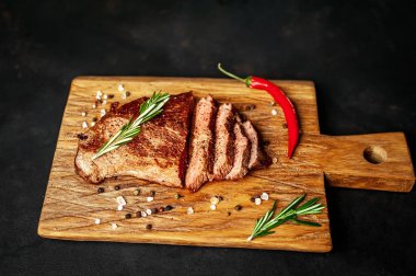 Siyah taş arka plan üzerinde ahşap doğrama tahtası üzerinde baharat ve biberiye dalları ile Taze ızgara domuz biftek