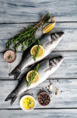 Gri ahşap arka plan üzerinde limon dilimleri ve biberiye dalları ile çiğ balık