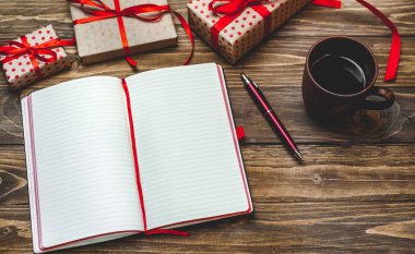 Eski ahşap arka plan üzerinde kırmızı yay ve boş defter ile hediye kutuları yığını 