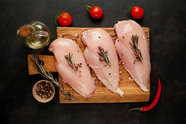 Ahşap doğrama tahtasında tuz, biberiye dalları ve zeytinyağı şişesi ile çiğ tavuk fileto