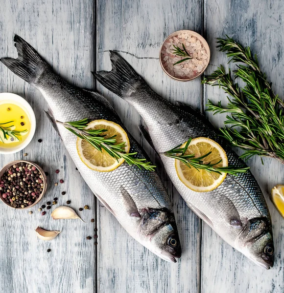 Gri ahşap arka plan üzerinde limon dilimleri ve biberiye dalları ile çiğ balık