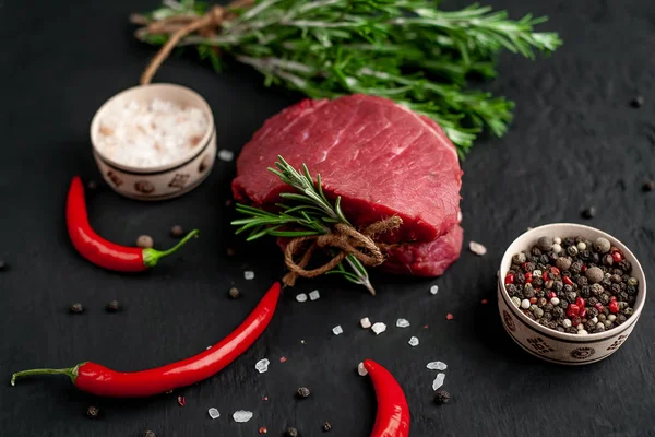 Siyah taş arka plan üzerinde yeşil biberiye dalları ve baharatlar ile Çiğ biftek 