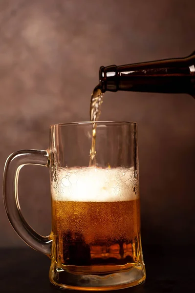Golden beer pouring in glass on brown stone background