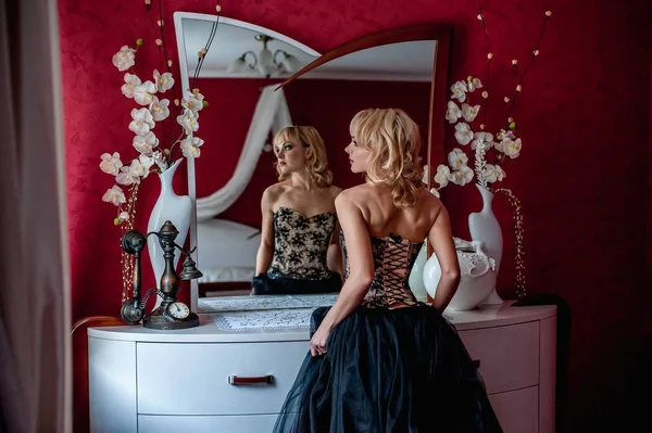 Zarif gece elbisesi giymiş genç sarışın kadın aynanın önünde poz veriyor. 