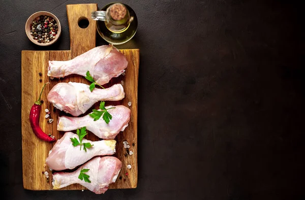 Siyah taş arka plan üzerinde ahşap doğrama tahtası üzerinde baharat, tuz, maydanoz yaprakları ve yağ şişesi ile Tavuk bacakları