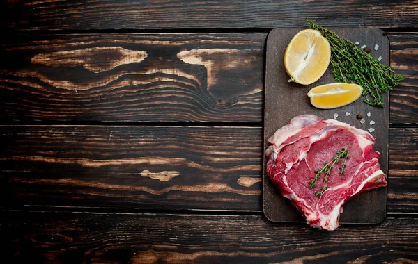 Ahşap arka plan üzerinde biberiye ve limon dilimleri ile Çiğ yağ domuz biftek 