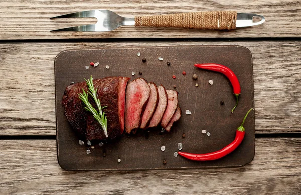 Ahşap arka planda baharat ve biberiye dalları ile taze ızgara biftek