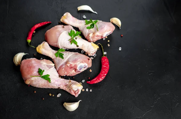 Chicken legs with spices, chili peppers and parsley leaves on black stone background