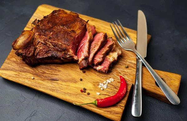 Siyah taş arka plan üzerinde doğrama tahtası üzerinde baharat ve biber ile Yağlı ızgara domuz biftek