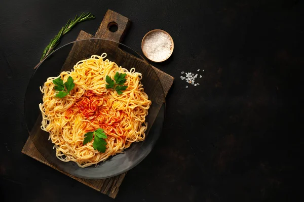 italian spaghetti pasta with tomato sauce and parsley leaves on dark stone background