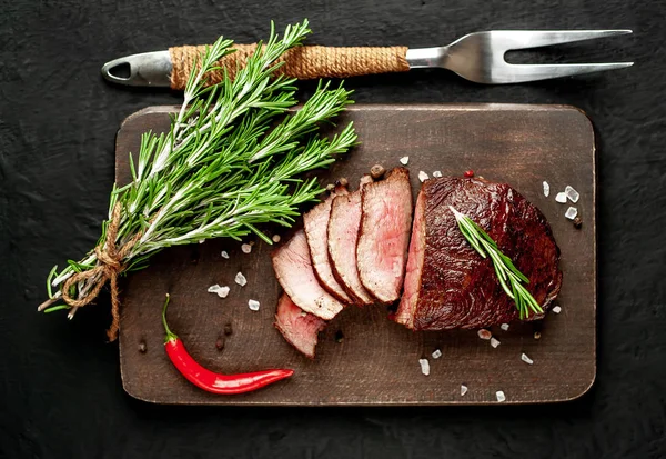 Siyah taş arka plan üzerinde baharat ve biberiye dalları ile Taze ızgara biftek