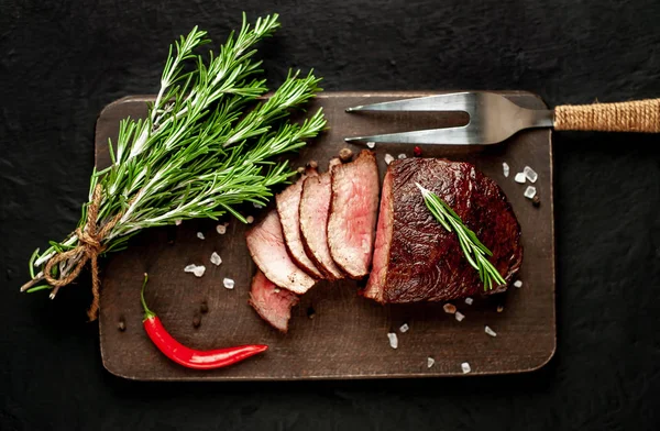 Siyah taş arka plan üzerinde baharat ve biberiye dalları ile Taze ızgara biftek