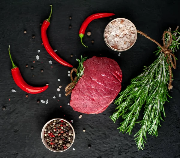 Siyah taş arka plan üzerinde yeşil biberiye dalları ve baharatlar ile Çiğ biftek 