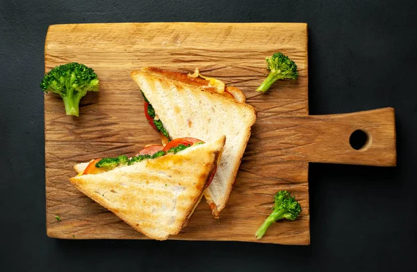 Ahşap doğrama tahtasında jambon, taze brokoli ve peynirile taze ızgara sandviçler