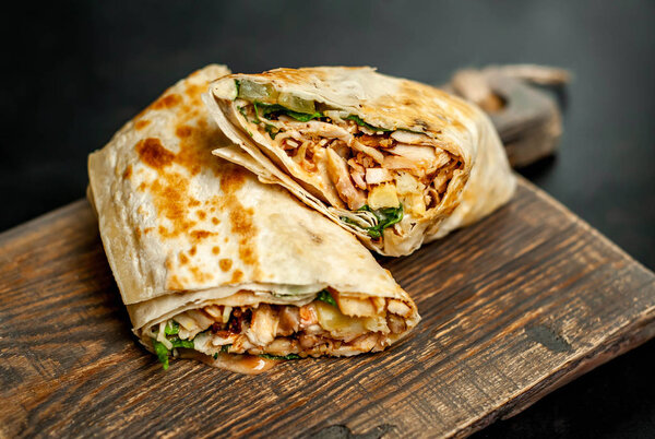 Homemade mexican burrito wrapped with chicken and vegetables on wooden chopping board 