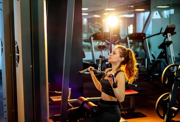 Young sporty woman training muscles at empty gym