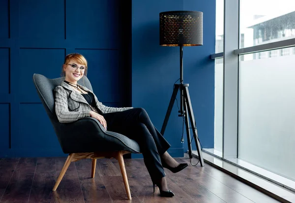 Elegant businesswoman sitting in armchair in blue studio