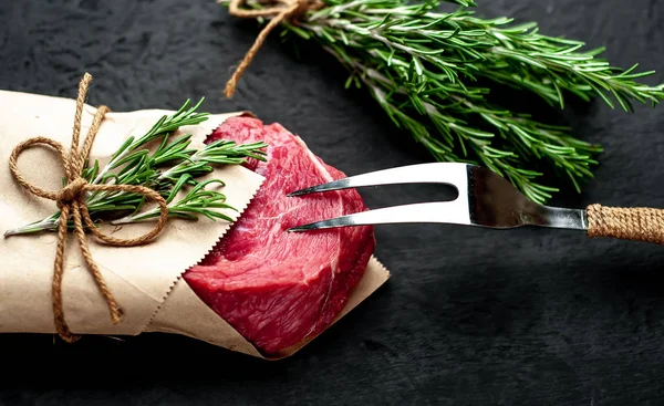 Çiğ sığır eti biftek taş arka plan üzerinde biberiye dalları ile zanaat kağıt sarılmış 