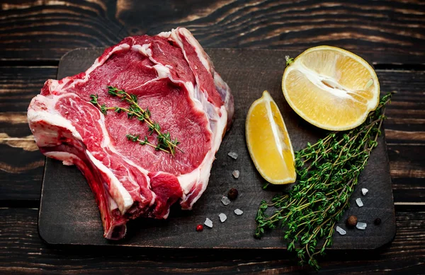 Ahşap arka plan üzerinde biberiye ve limon dilimleri ile Çiğ yağ domuz biftek 