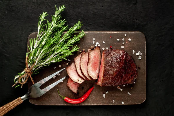 Siyah taş arka plan üzerinde baharat ve biberiye dalları ile Taze ızgara biftek