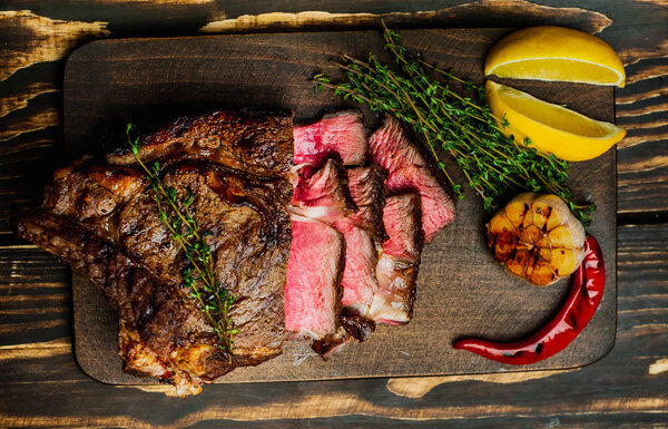 Fresh roasted steak served with lemon slices and grilled garlic on wooden chopping board