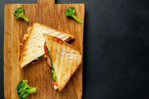 Ahşap doğrama tahtasında jambon, taze brokoli ve peynirile taze ızgara sandviçler