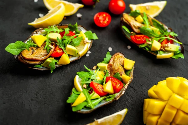 Siyah beton arka plan üzerinde avokado, arugula, mango, domates ve limon dilimleri ile pişmiş midye