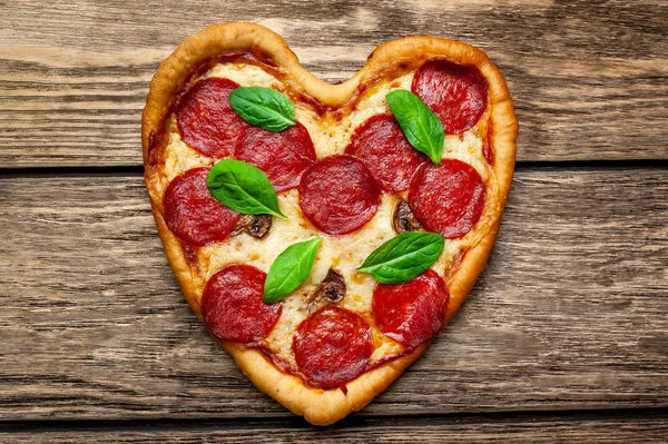 ahşap arka plan üzerinde salam ve taze fesleğen yaprakları ile peynir kalp pizza