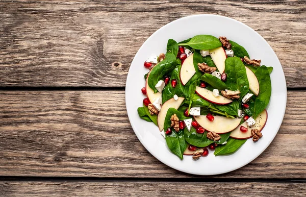 Ahşap arka plan üzerinde ıspanak yaprakları, peynir, nar tohumu, elma dilimleri ve fındık ile taze salata 