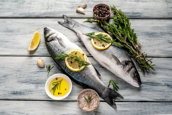 Gri ahşap arka plan üzerinde limon dilimleri ve biberiye dalları ile çiğ balık