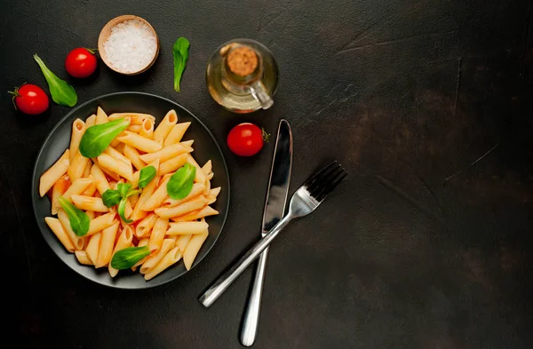 domates soslu makarna, yeşil yapraklar ve taş siyah arka plan üzerinde olgun domates