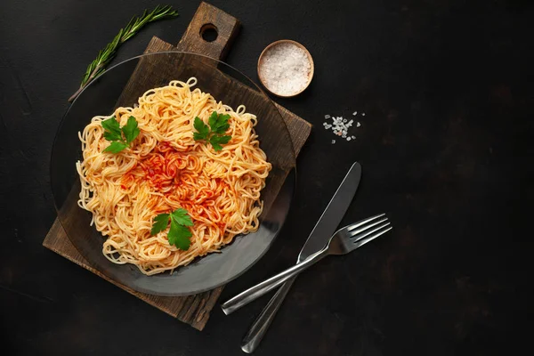 koyu taş arka plan üzerinde domates sosu ve maydanoz yaprakları ile İtalyan spagetti makarna