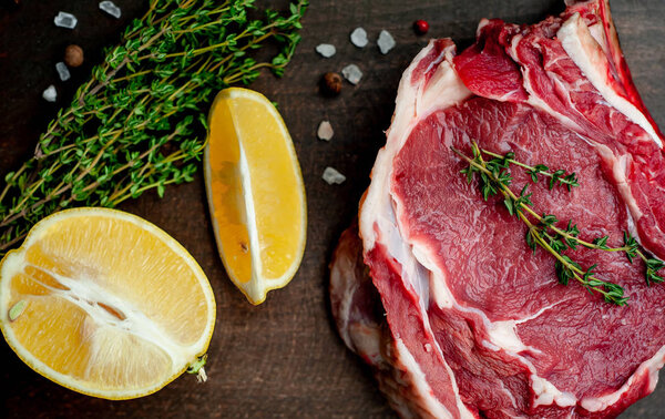 Raw fat pork steak with rosemary and lemon slices on wooden background 
